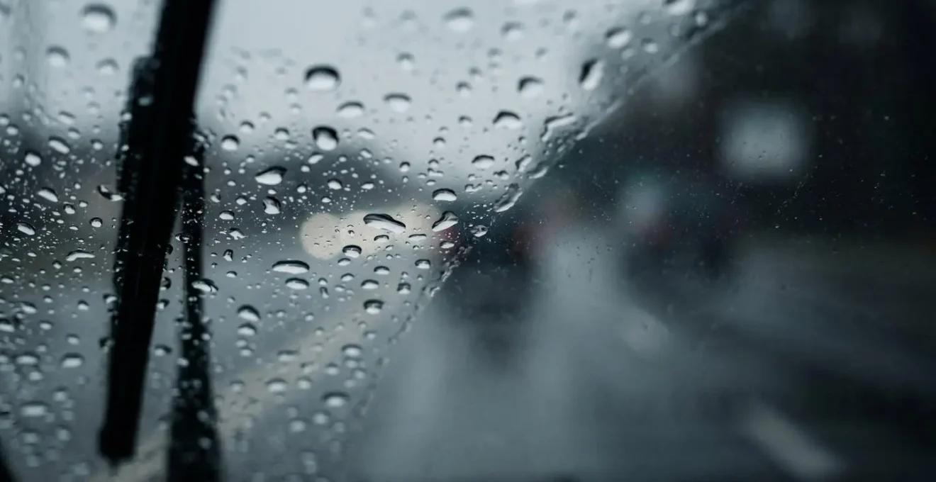 Gouttelettes de pluie sur pare-brise avec système d'essuie-glace en action et route mouillée visible