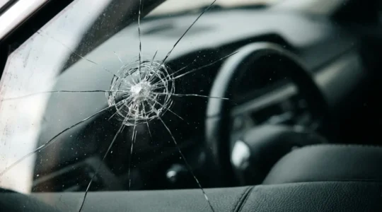 Gros plan dramatique sur un pare-brise de voiture fissuré avec un petit impact étoilé, en lumière naturelle diffuse