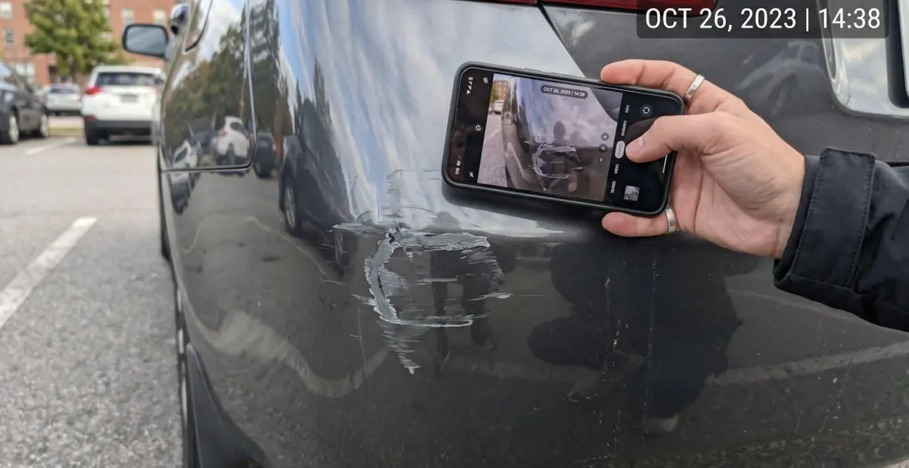 Main tenant un smartphone prenant une photo détaillée d'une rayure sur la carrosserie d'un véhicule avec horodatage visible
