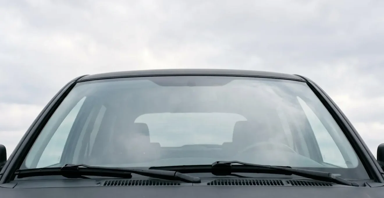 Vue environnementale d'un pare-brise de voiture avec zones critiques de fragilité près des bords et essuie-glaces